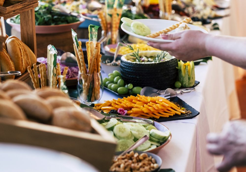 Close up of catering service table full of food and people serving and taking on dishes.